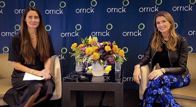 Jen in. front of Orrick branded backdrop with a book tour moderator