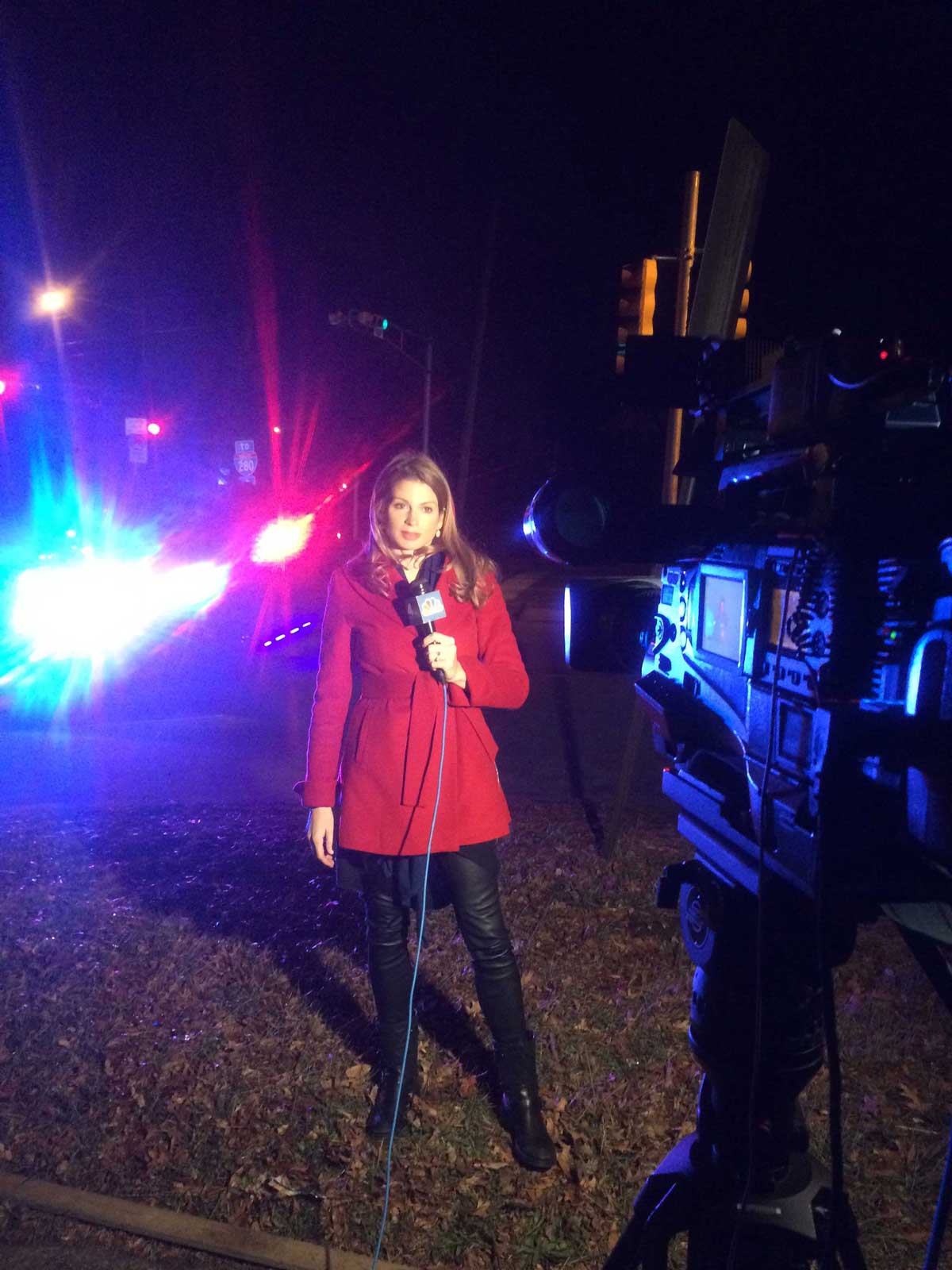 Jen in the field at night, reporting on a crime scene in a red wrap coat.